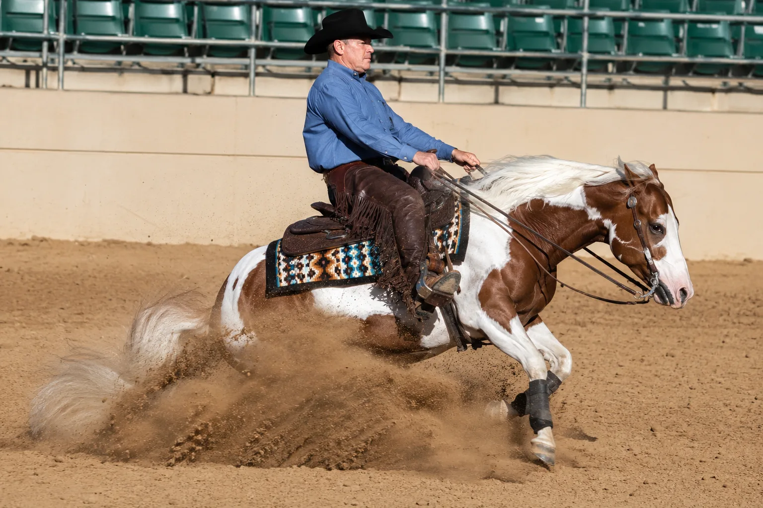 American Paint Horse in voller Aktion bei einem Reining-Slide-Stop, Staub in einer Arena aufwirbelnd, mit einem Westernreiter.